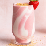 a glass of strawberry cheesecake smoothie with graham cracker crumbs and a fresh strawberry on the rim of the glass.