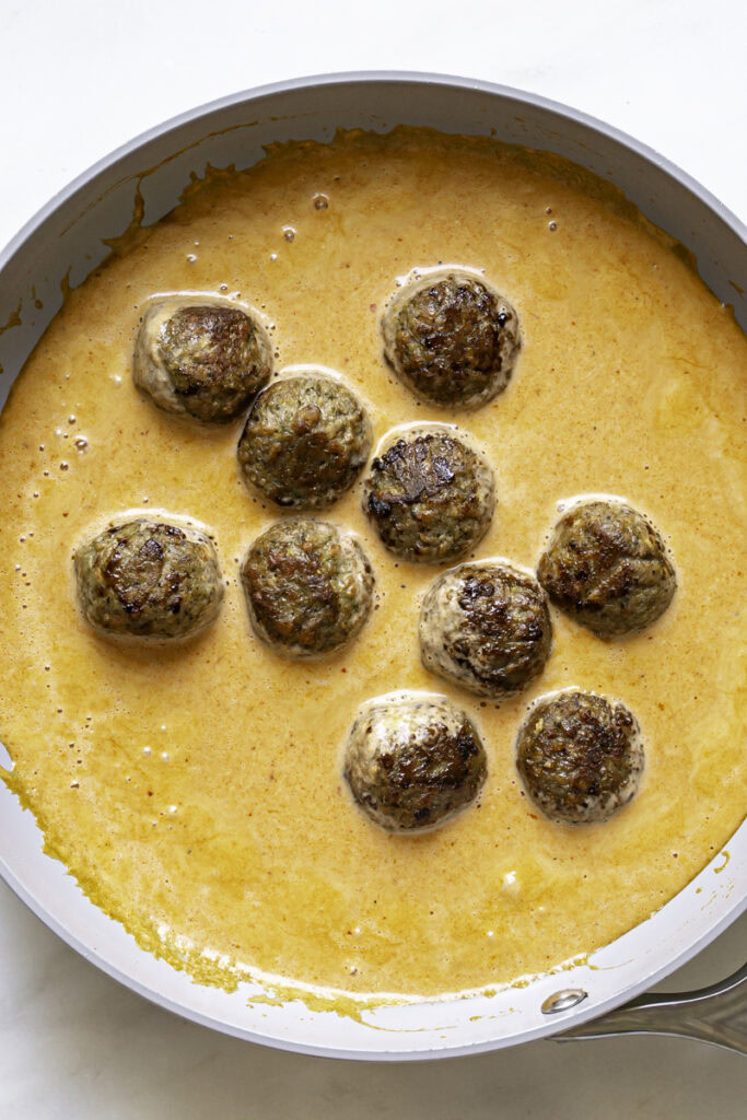 cooked vegan meatballs added to the skillet with the coconut curry sauce in a skillet.