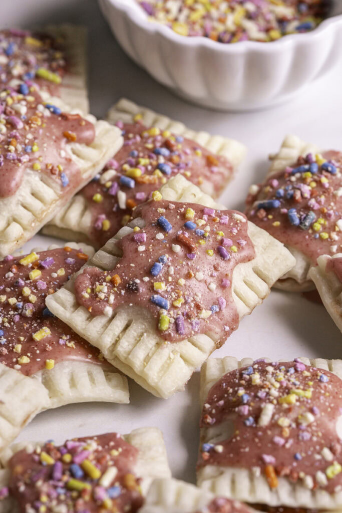 3/4 image of mini strawberry chia pop tarts piled on top of one another with a bowl of sprinkles in the background.