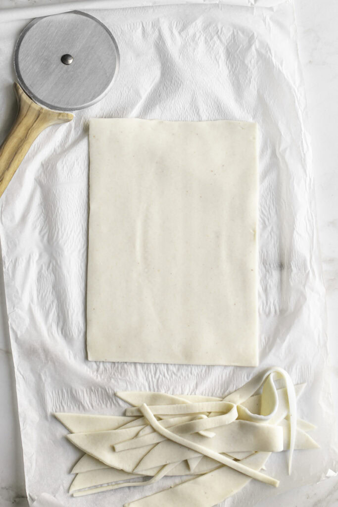 slicing pie crust into a large rectangle with a pizza cutter.