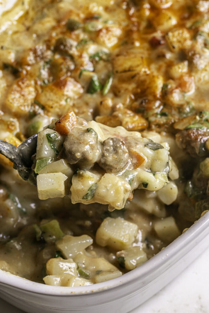close up of spooning some creamy vegan breakfast hashbrown casserole out of the casserole dish with a spoon.