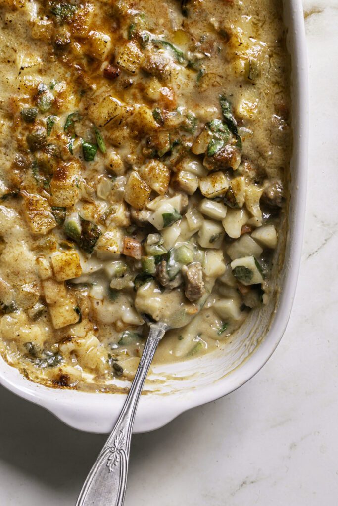 creamy vegan breakfast hashbrown casserole in a casserole dish with a spoon.
