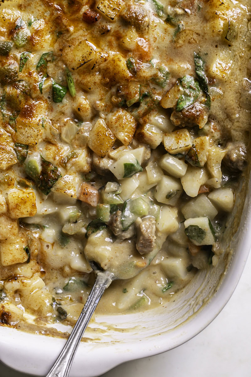 creamy vegan breakfast hashbrown casserole in a casserole dish with a spoon.