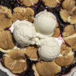 baked cookie berry cobbler with 3 scoops of vanilla ice cream on top.
