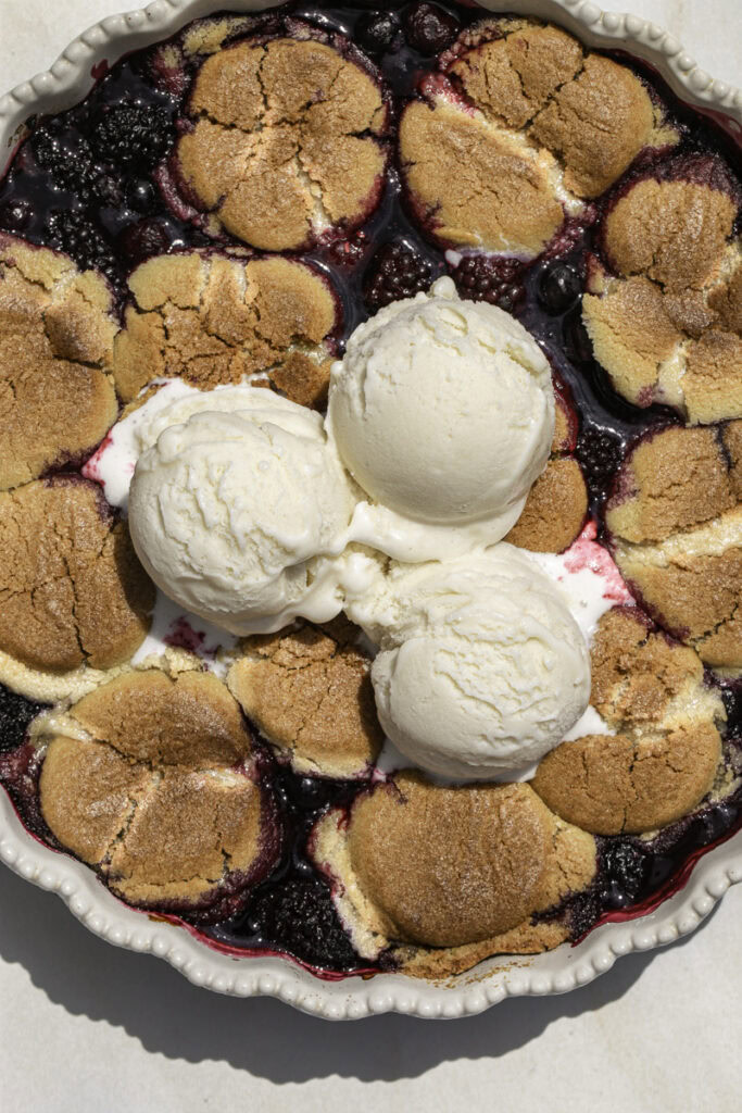 baked cookie berry cobbler with 3 scoops of vanilla ice cream on top.