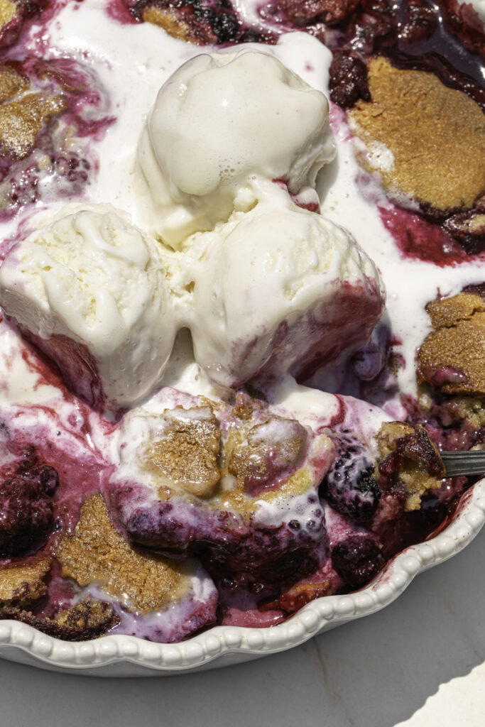 close up of cookie berry cobbler with melting vanilla ice cream on top.
