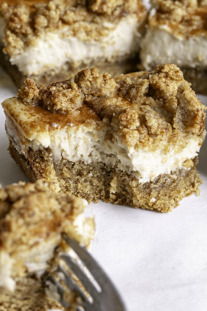 a close up of Cinnamon cookie cheesecake crumb bar, and a fork taking a piece off.