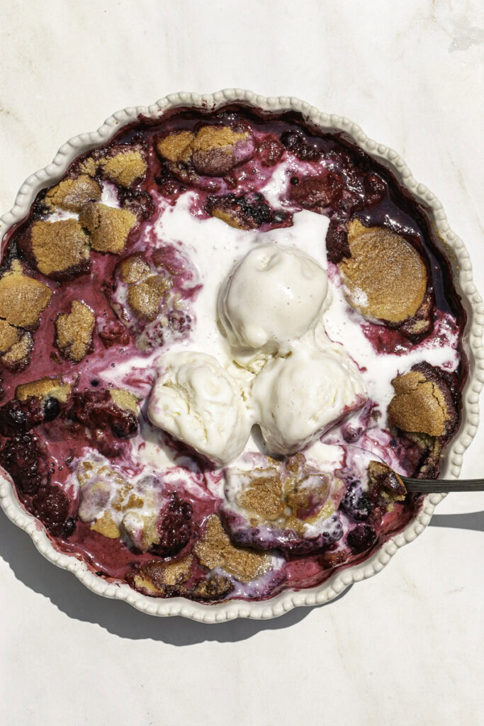 cookie berry cobbler with melting vanilla ice cream on top and a spoon in the dish.