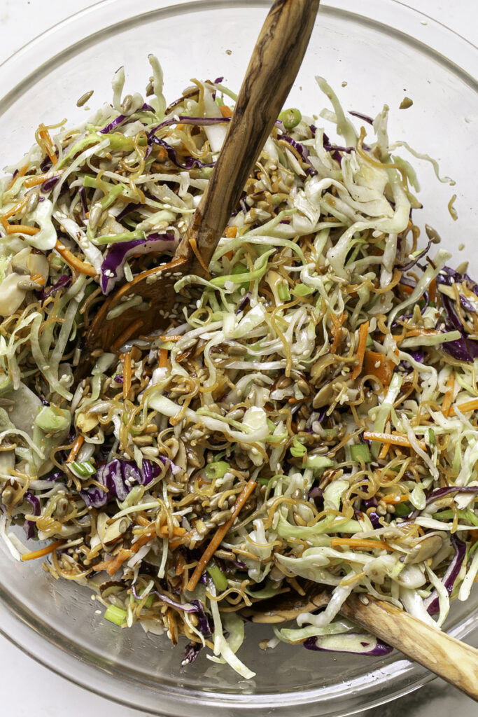 crunchy ramen noodle cabbage salad mixed with the dressing in the large bowl, with wooden salad tongs in the bowl.