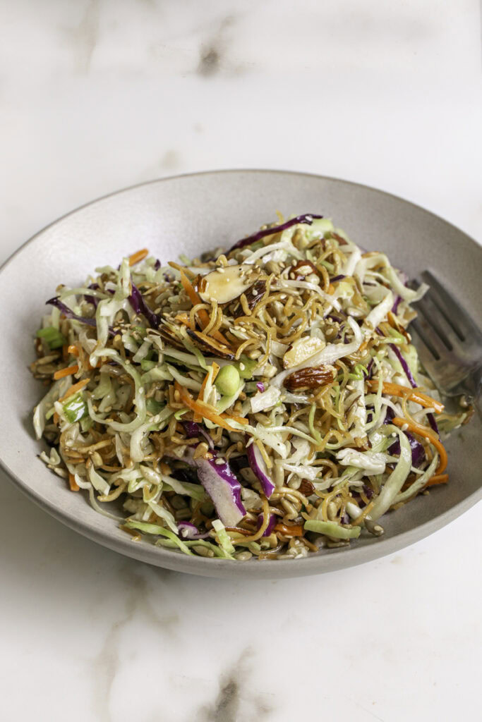 a bowl of crunchy ramen noodle cabbage salad with a fork.