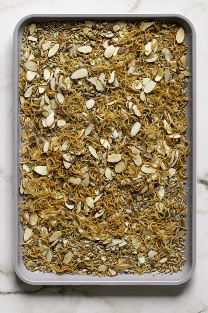 baked ramen noodles, sliced almonds, sesame seeds, and sunflower seeds on a baking sheet.