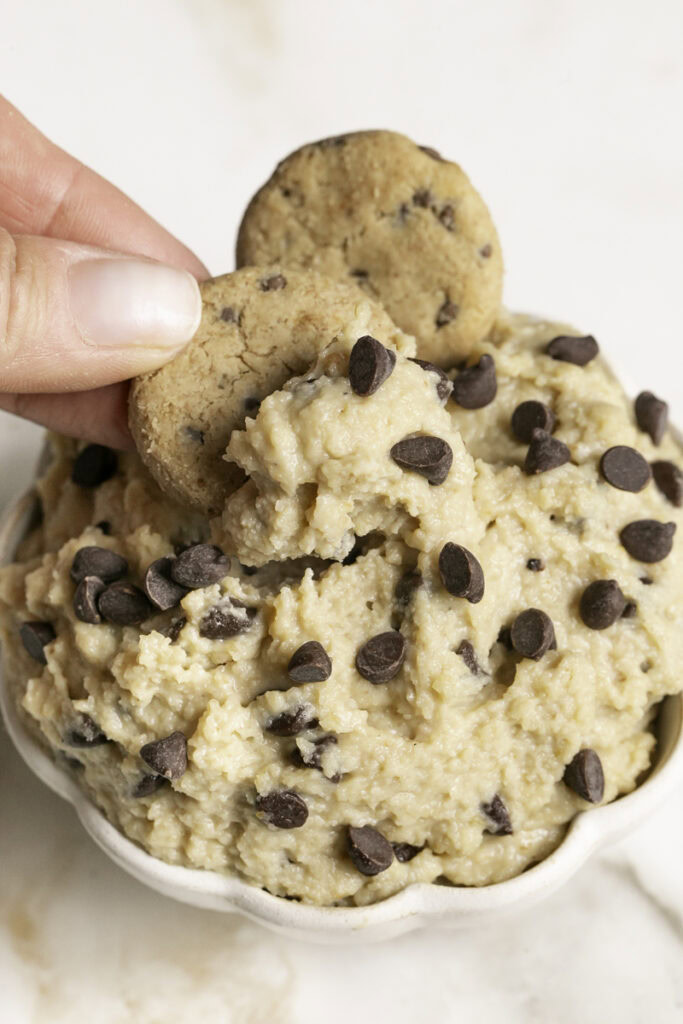 action shot dipping a mini chocolate chip cookie in the cookie dough dip.