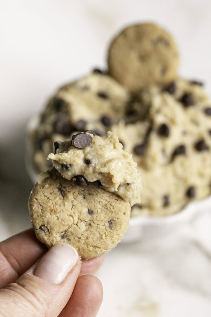 close up of the cookie dough dip on a mini chocolate chip cookie with the dip in the background.
