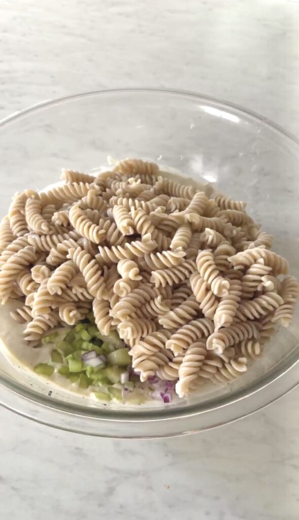 cooked pasta added to the bowl with the chopped produce and dressing.