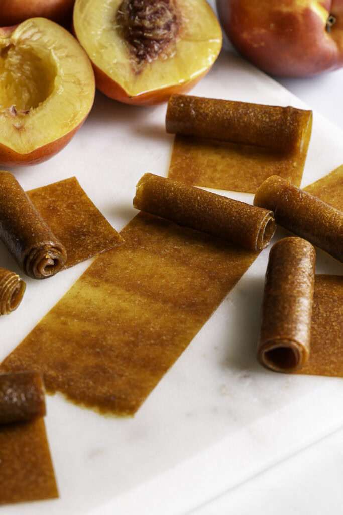 half rolled up nectarine fruit leather with fresh nectarines in the background.