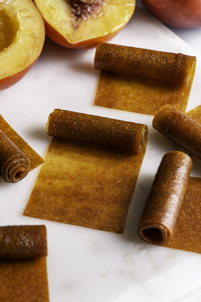 half rolled up nectarine fruit leather with fresh nectarines in the background.