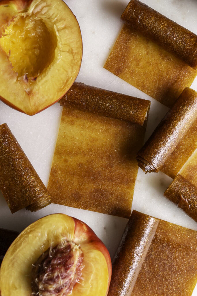 overhead shot of half rolled up nectarine fruit leather with a fresh sliced in half nectarine.