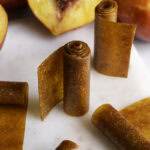 rolled up nectarine fruit leather, some rolls standing vertically, some laying down. Fresh nectarines in the background.