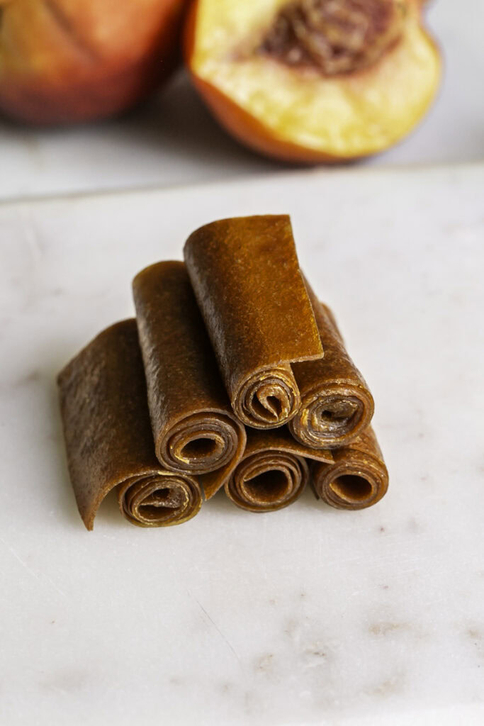 6 nectarine fruit rollups stacked on top of one another with a fresh nectarine in the background.