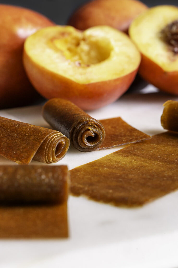 rolled nectarine fruit leather, some unrolled halfway with fresh nectarines in the background.