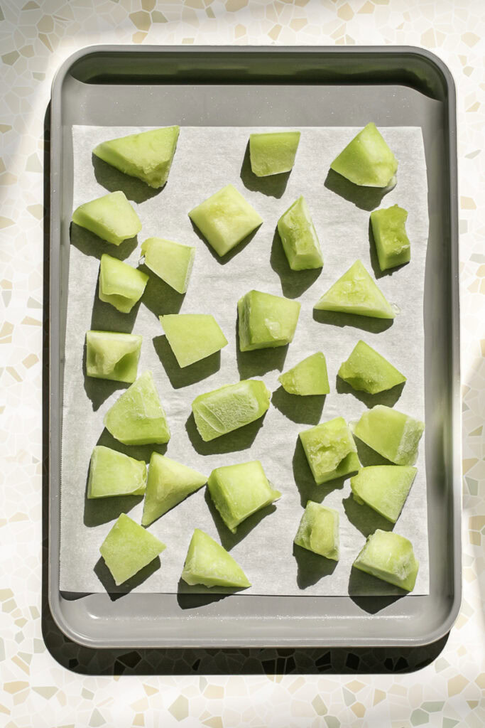 frozen honeydew pieces on a parchment-lined baking sheet.