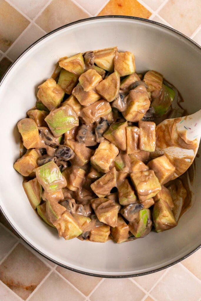 apples and dates mixed with the date yogurt dressing in a mixing bowl.