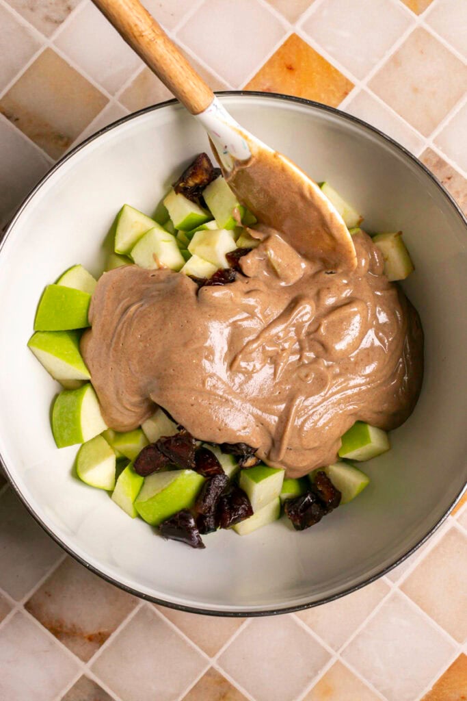 chopped green apple, chopped dates, date yogurt dressing in a mixing bowl with a spatula.