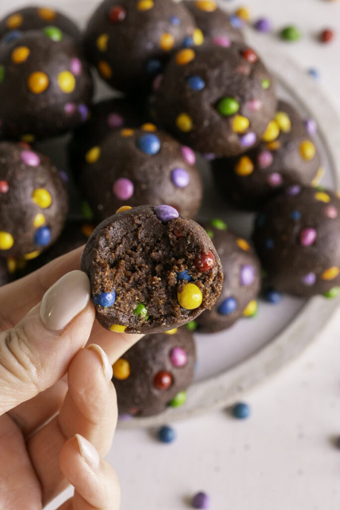 a hand holding a Cosmic Brownie Cookie Dough Date Bite with a bite taken out of it.