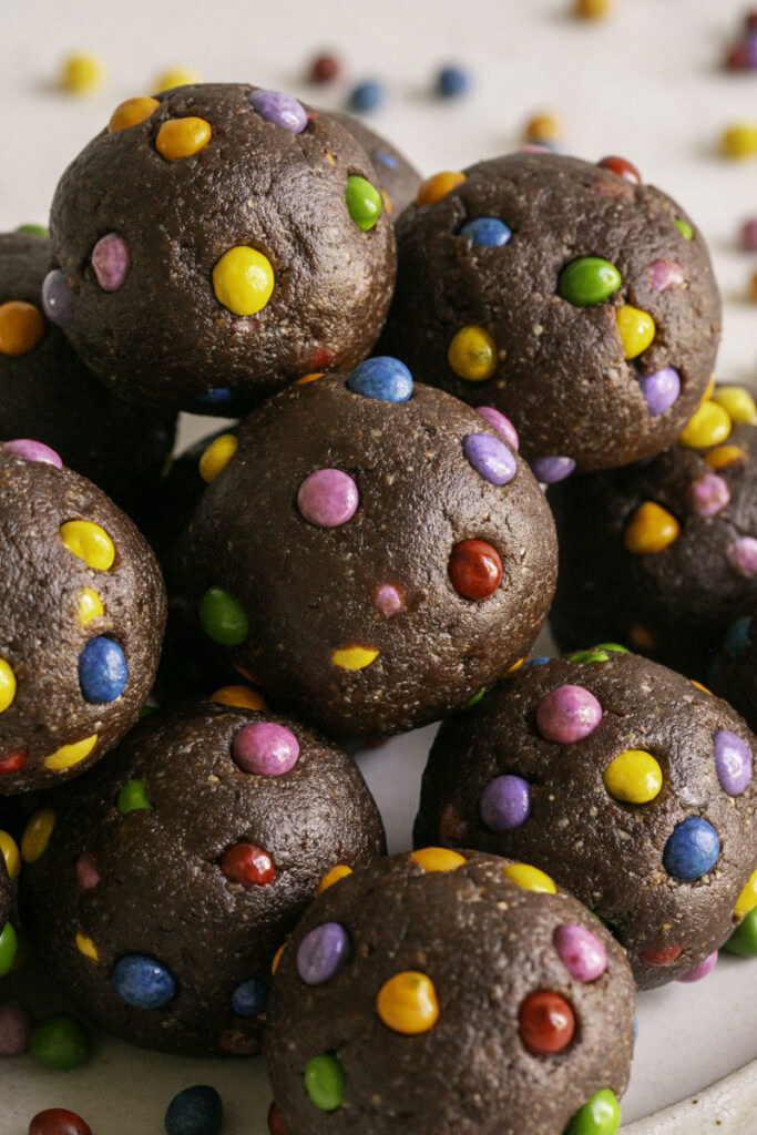 close up of no-bake cosmic brownie cookie dough dates bites stacked on top of one another.