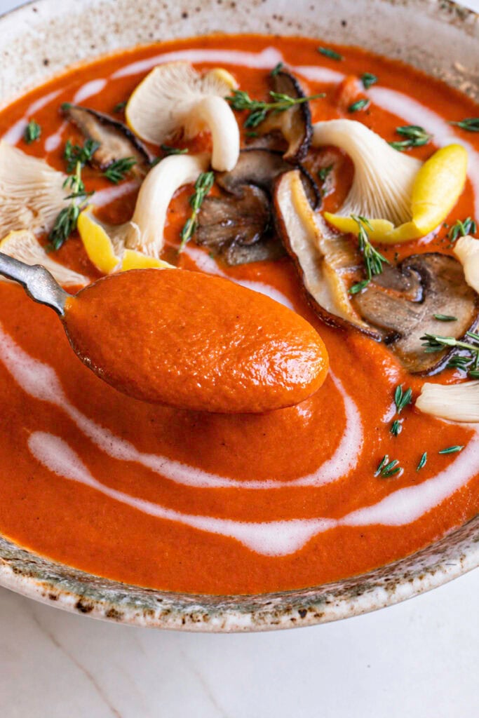 action shot scooping some Creamy Mushroom Tomato Bisque soup with a spoon.