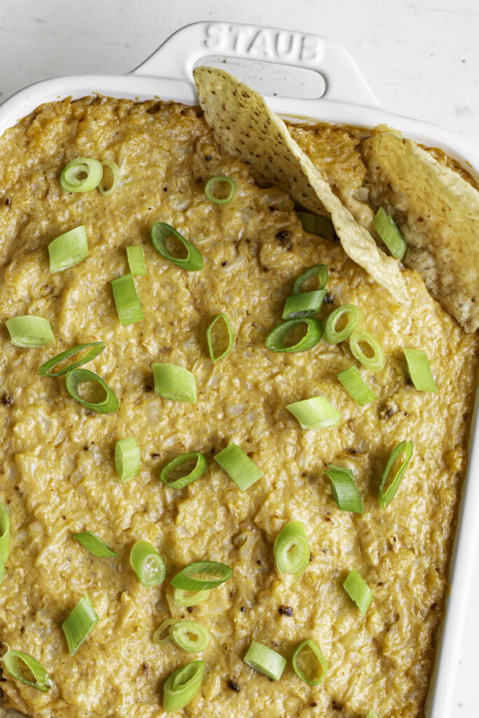 close up of baked buffalo cauliflower dip with tortilla chips in the corner of the dip.