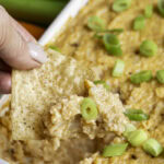 action shot scooping out some of the buffalo cauliflower dip with a tortilla chip.