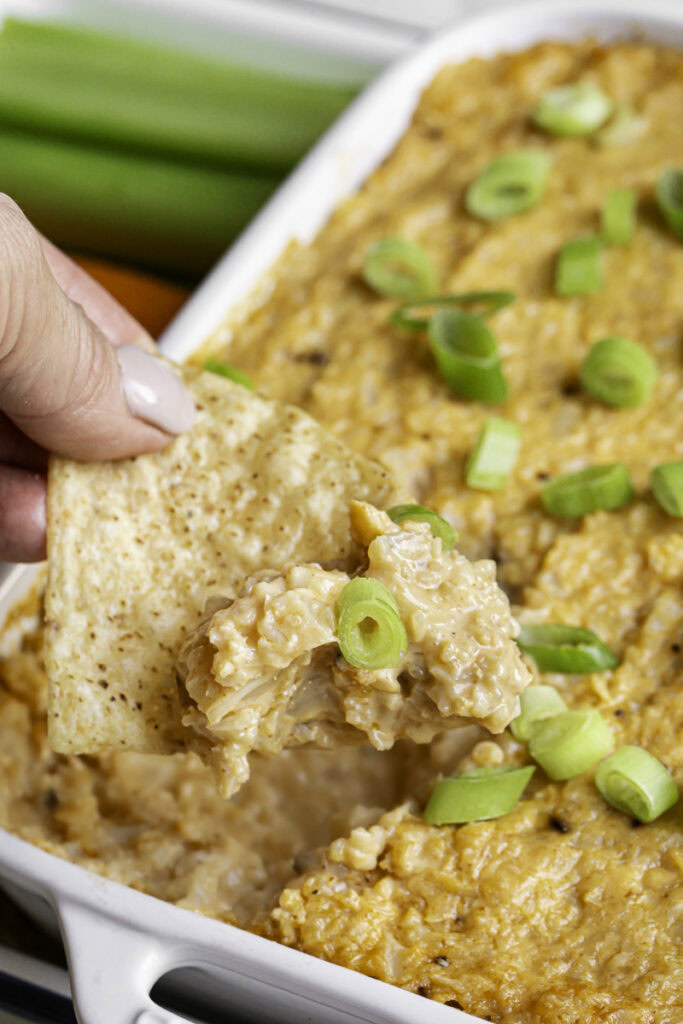 action shot scooping out some of the buffalo cauliflower dip with a tortilla chip.
