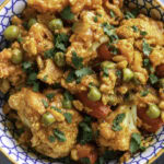 Curried cauliflower with tofu, peas, and red bell peppers in a decorative bowl.