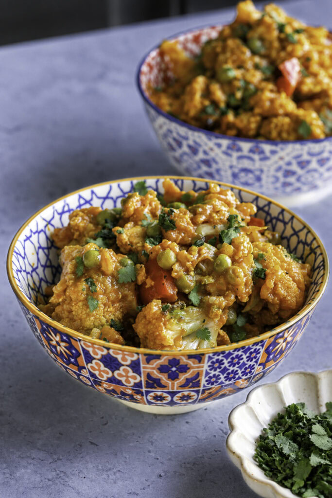 Healthy cauliflower and tofu curry with red bell peppers and peas in decorative bowls.