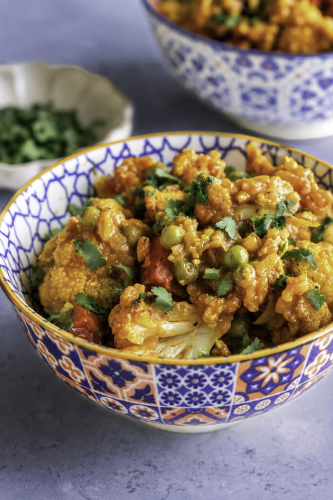 Vibrant curried cauliflower with tofu, peas, and red bell peppers in a decorative bowl.