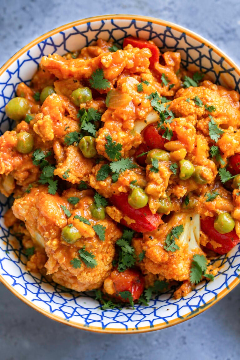 Curried cauliflower with tofu, peas, and red bell peppers in a decorative bowl.