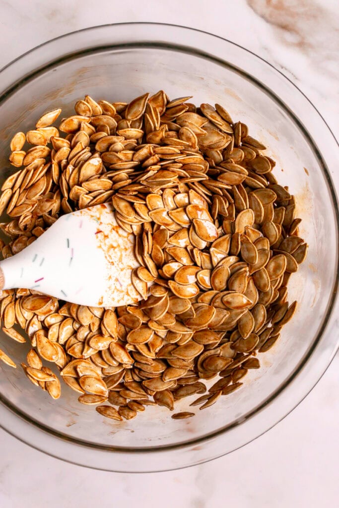 pumpkin seeds in a glass bowl mixed with the maple cinnamon sugar butter coating.