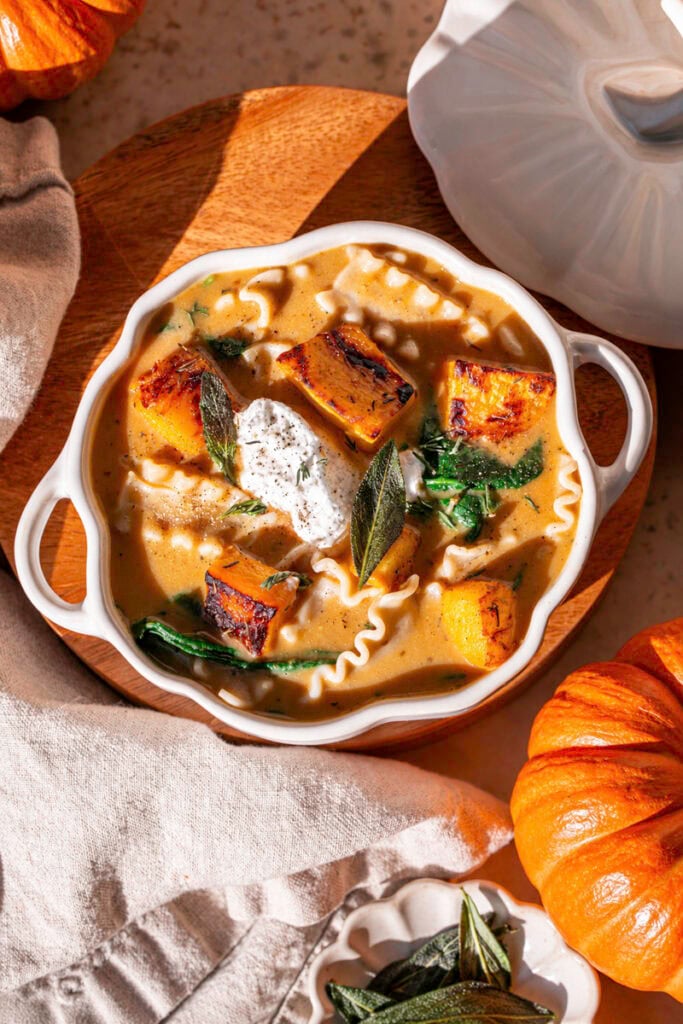 overhead shot of Creamy Roasted Pumpkin Lasagna Soup with a mini orange pumpkin and napkin.
